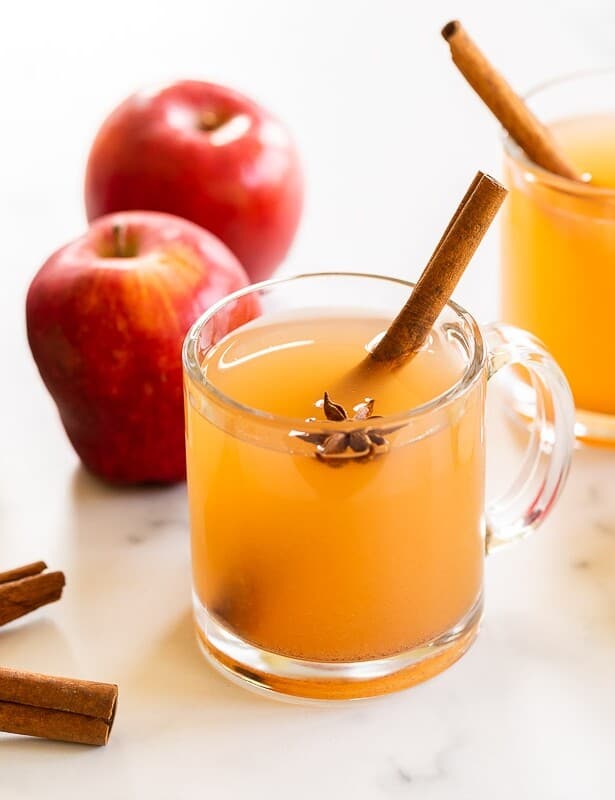 一个大理石表面，用透明的杯子装满自制苹果酒，整个苹果和肉桂棒到侧面。