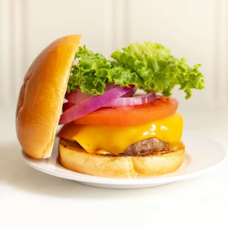 有多汁汉堡的一块白色板材堆积用蕃茄，莴苣，葱和乳酪，倾斜反对堆的小圆面包顶部。GydF4y2Ba