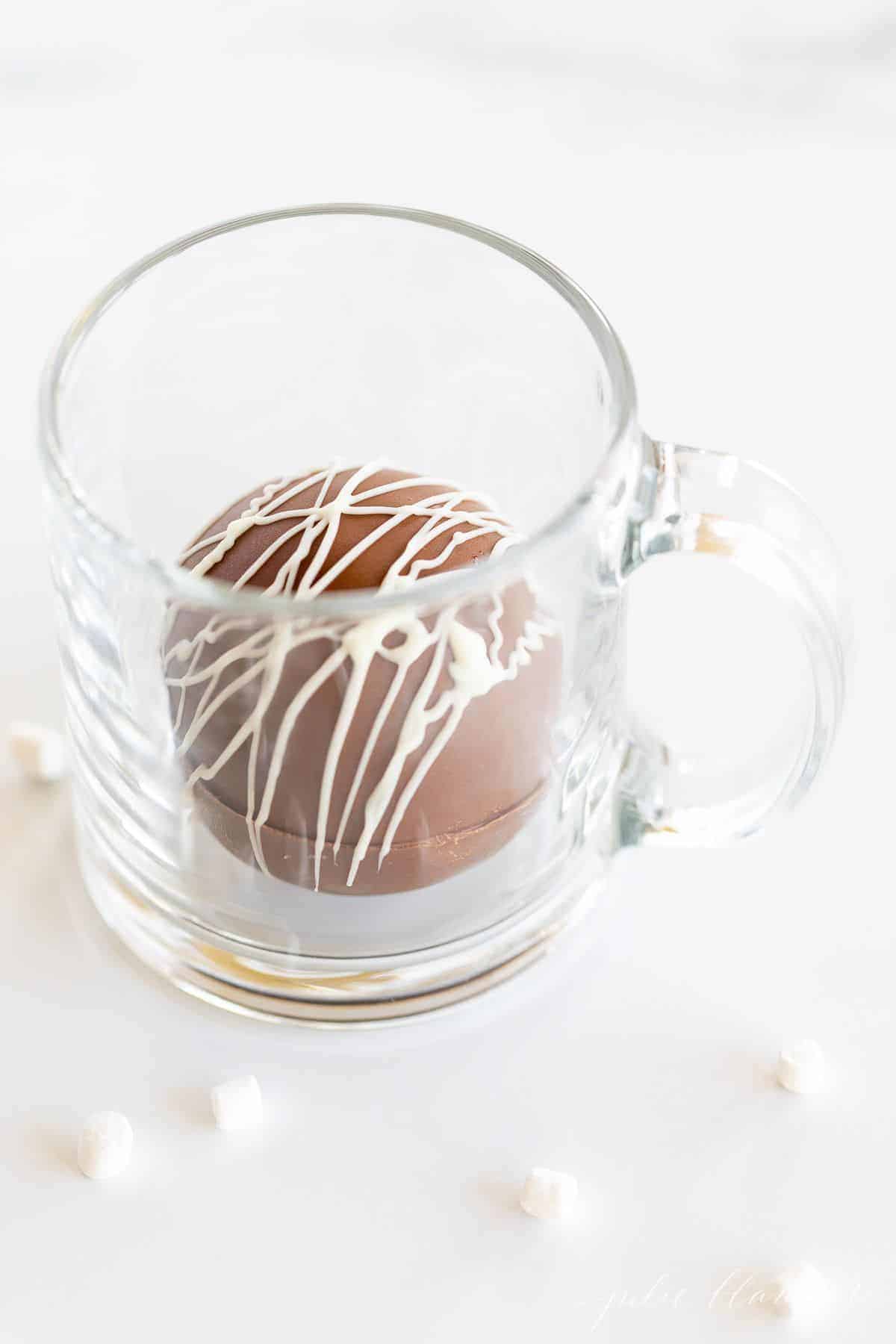 一个透明的玻璃杯子，里面有一个热巧克力炸弹，大理石表面的杯子周围有棉花糖。gydF4y2Ba