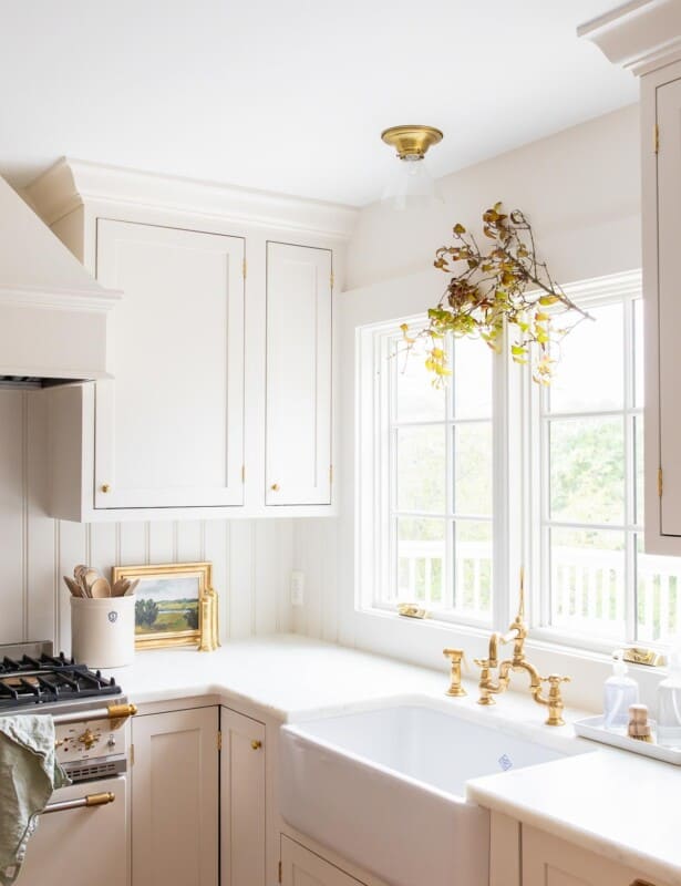 一个白色的厨房，上面有一个秋天的树枝悬挂在厨房的水槽窗户上。