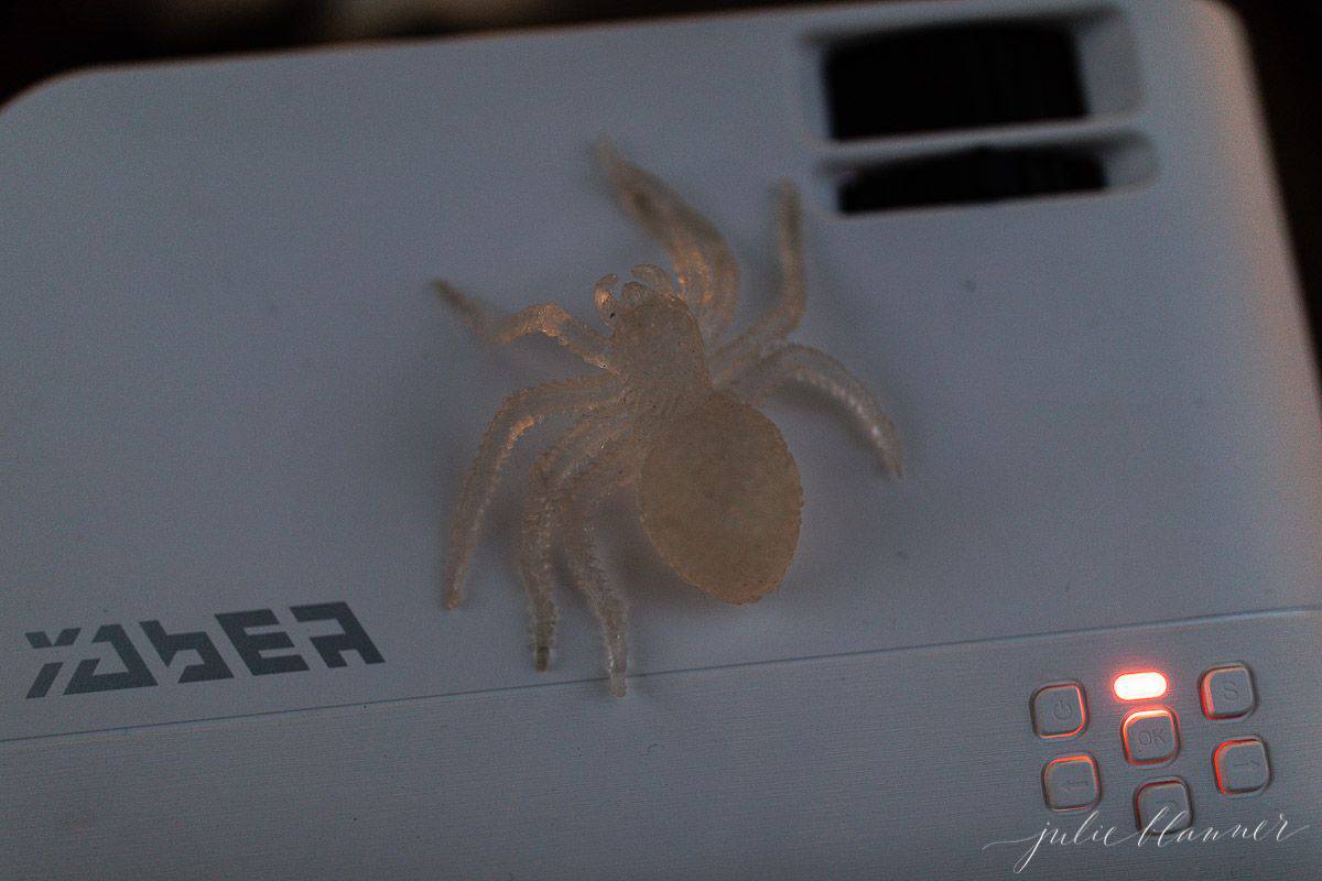 万圣节户外电影之夜的投影仪，上面有一只塑料蜘蛛。