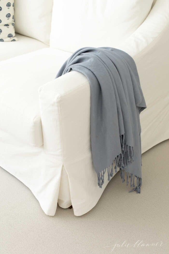 奶油色的室内室外地毯，看起来像剑麻，在白色沙发下，手臂上搭着一条蓝色的毯子。