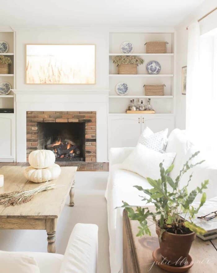 一个白色的客厅，带有壁炉，内置在书架上，并装饰着秋天的咖啡桌。