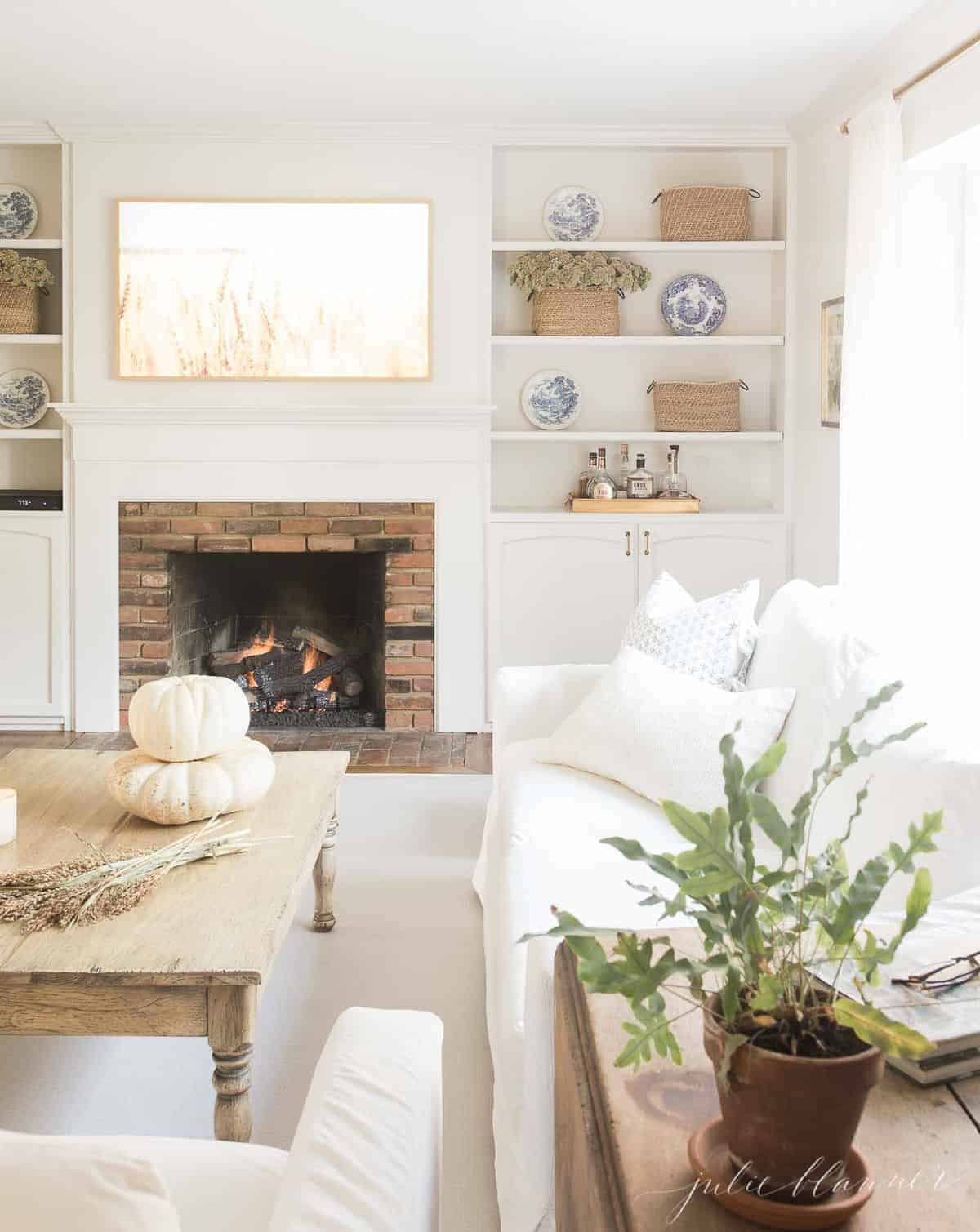 一个白色的客厅，有壁炉、架子和一张茶几，为秋天而装饰。
