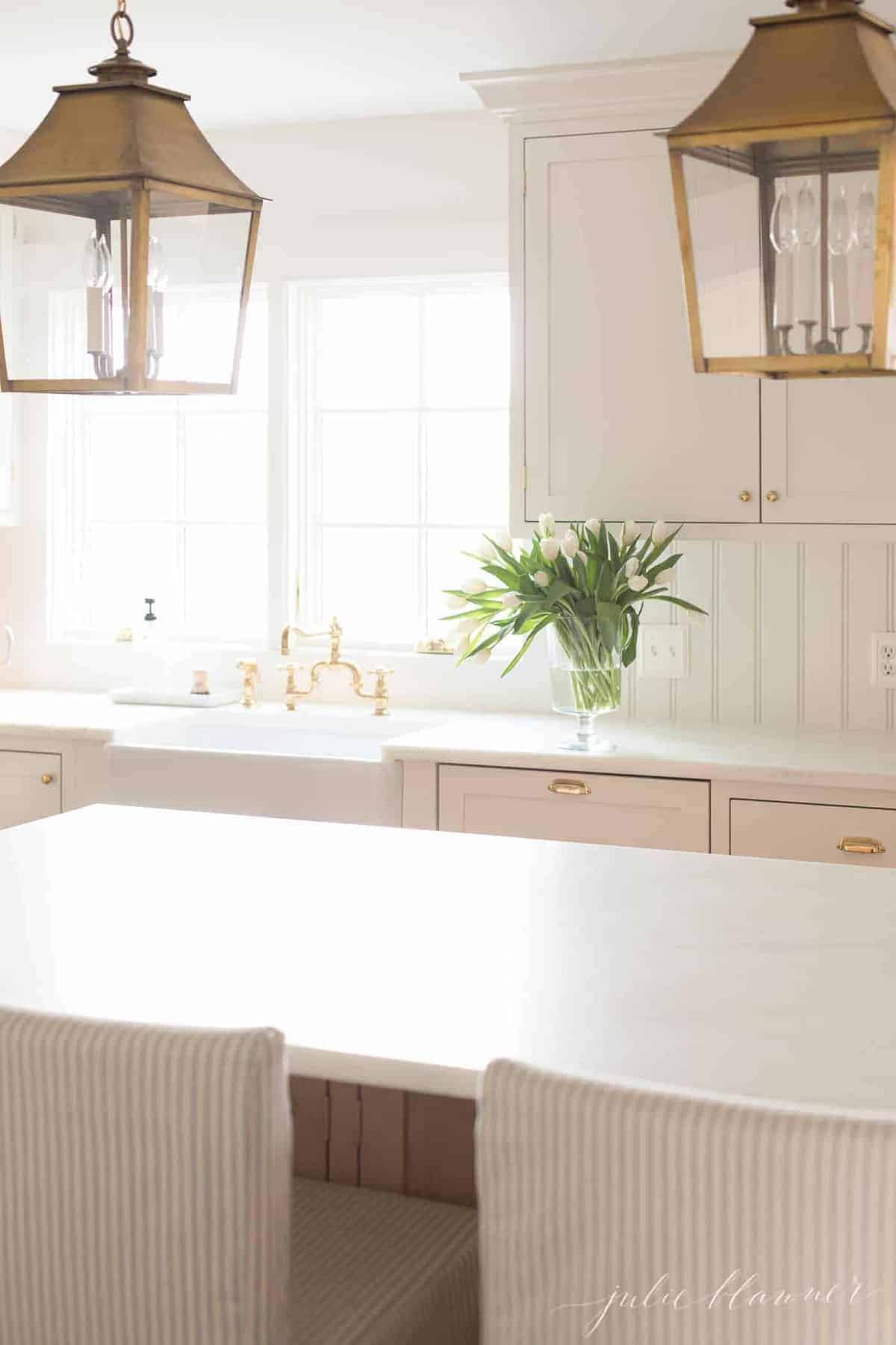 白色的厨房里有一个白色的大岛台，空无一物的极简主义美学，水池旁边有一个玻璃花瓶，里面种着郁金香。