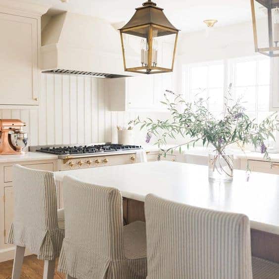 一个白色的厨房，有三个高脚凳和一个装着野花的玻璃花瓶。