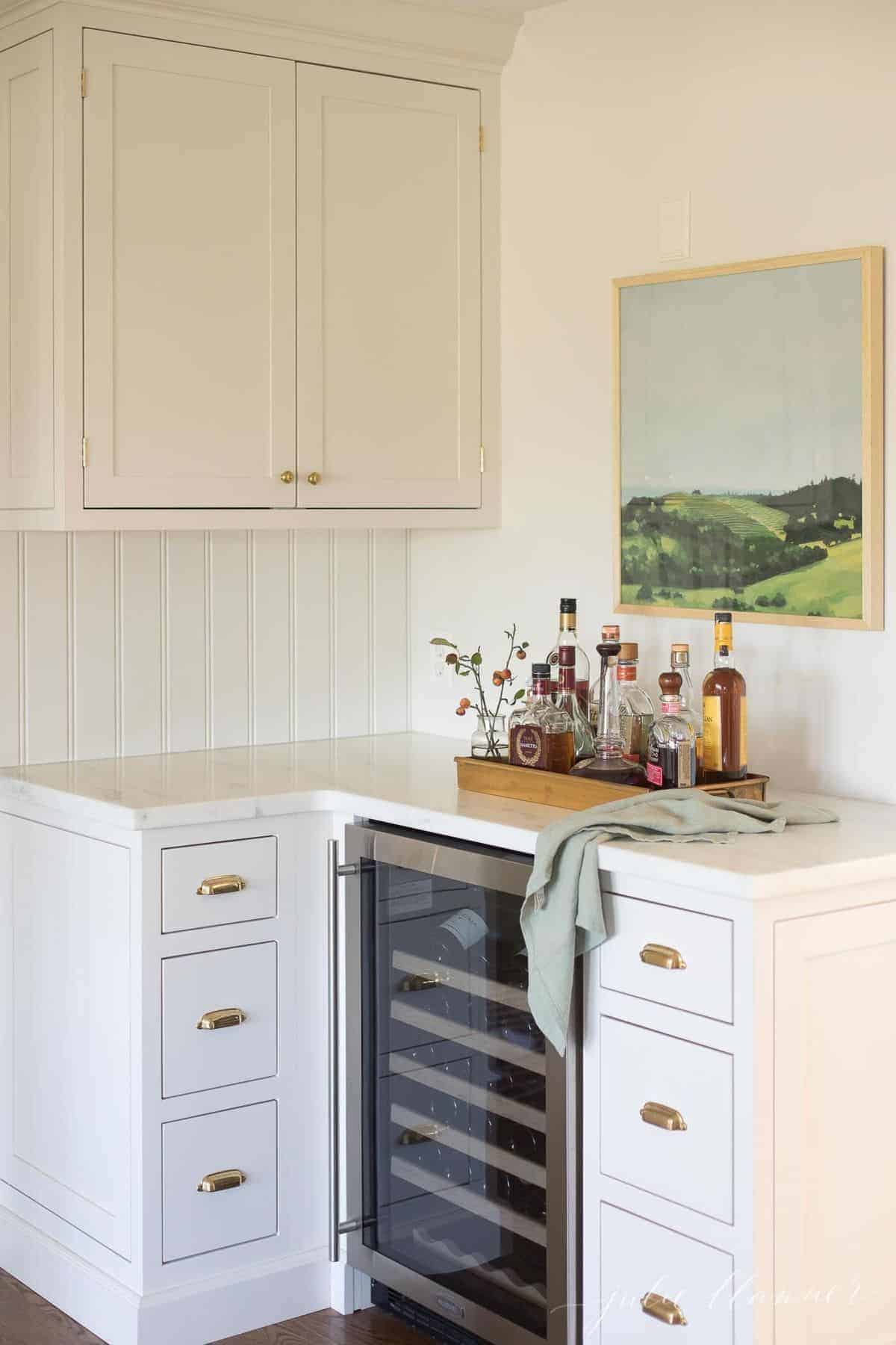一个白色厨房的角落，上面有一个小酒吧托盘，上面放着酒在葡萄酒冰箱上。