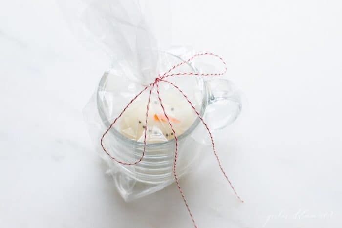 一个透明的杯子，里面有一个圣诞热巧克力炸弹，用玻璃纸和面包师的绳结包裹着。gydF4y2Ba