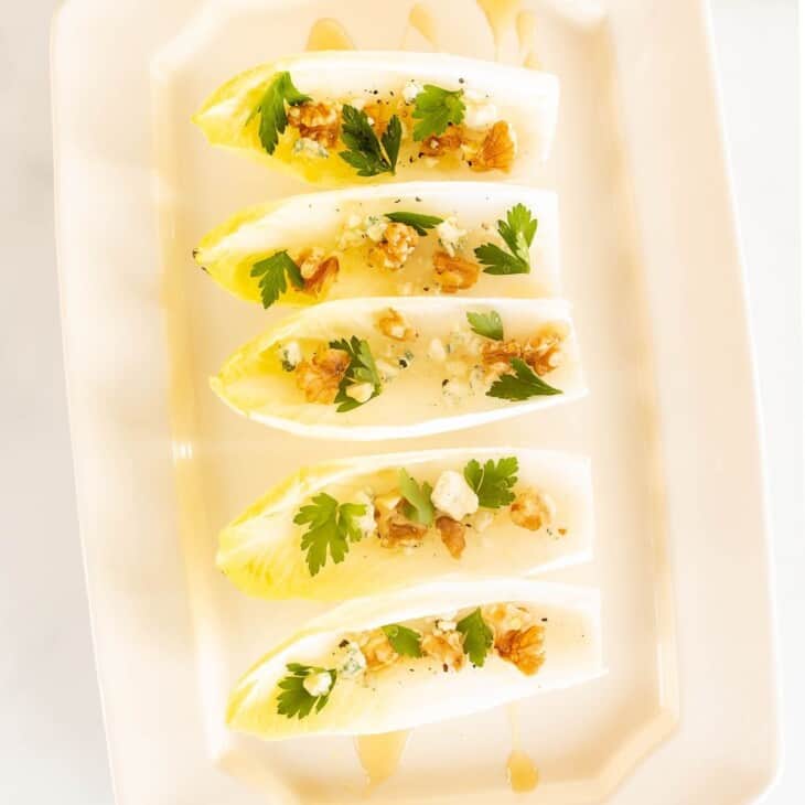 一个白色浅盘单独的菊苣莴苣叶，填满坚果，奶酪和更多菊苣沙拉开胃菜。gydF4y2Ba