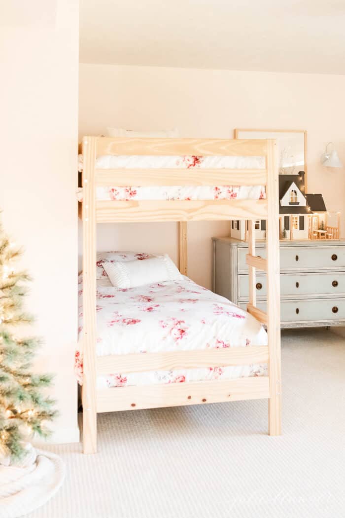 一个小女孩的房间，有双层床和一个蓝色的抽屉柜，上面有一个为圣诞节装饰的玩具屋。