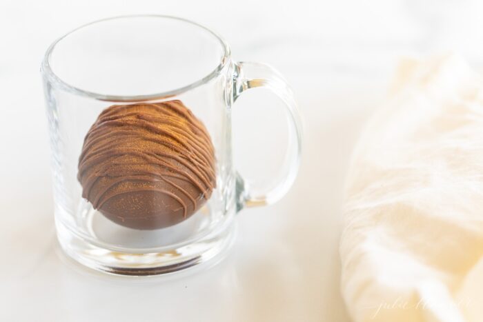 一个透明的杯子，里面有一个热辣的巧克力炸弹，肉桂棒和白色亚麻餐巾。gydF4y2Ba