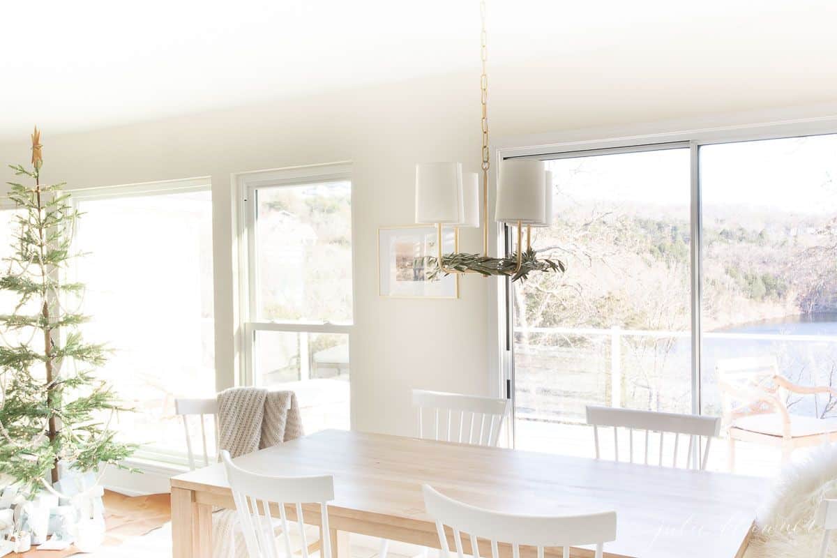 一张软木餐桌，配有白色的椅子，背景是一棵斯堪的纳维亚树，透过窗户可以看到湖景。