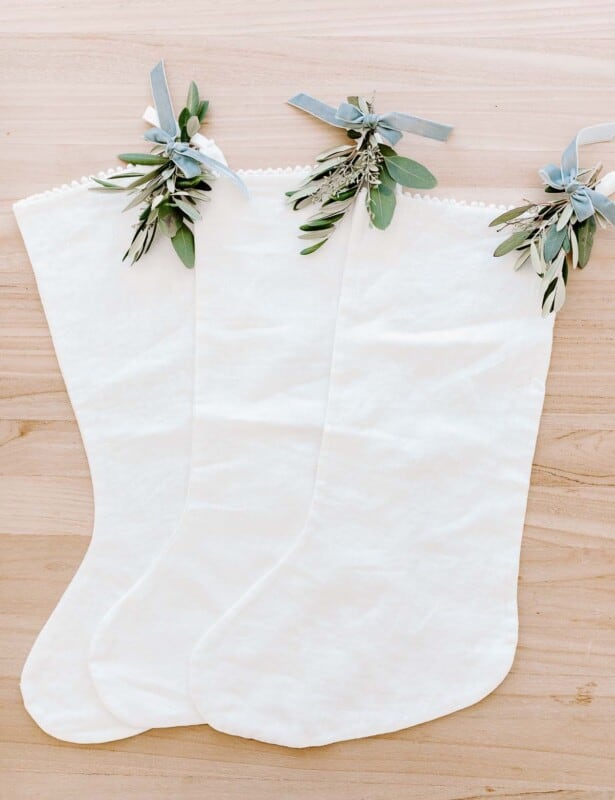 三个白色亚麻袜，带有节日绿化的触感，放在木质表面上。