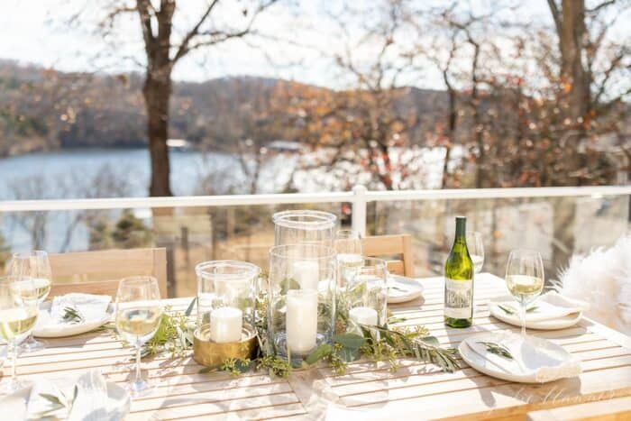 为圣诞晚餐设置的户外桌子，透明的玻璃飓风和绿色植物。