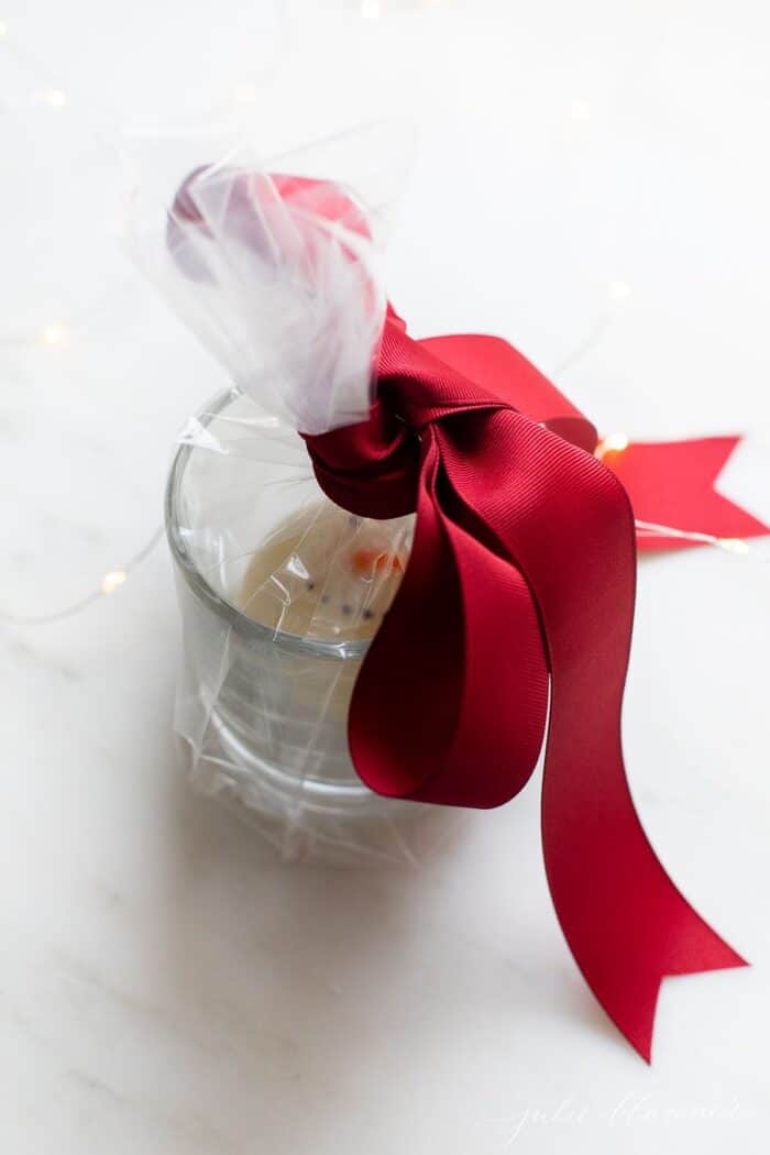 一个透明的杯子，里面有一个圣诞热巧克力炸弹，用玻璃纸包裹着，还有一个大大的红色蝴蝶结。gydF4y2Ba