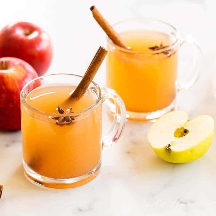 两个透明的玻璃杯装满了感恩节鸡尾酒，肉桂棒和苹果作为装饰