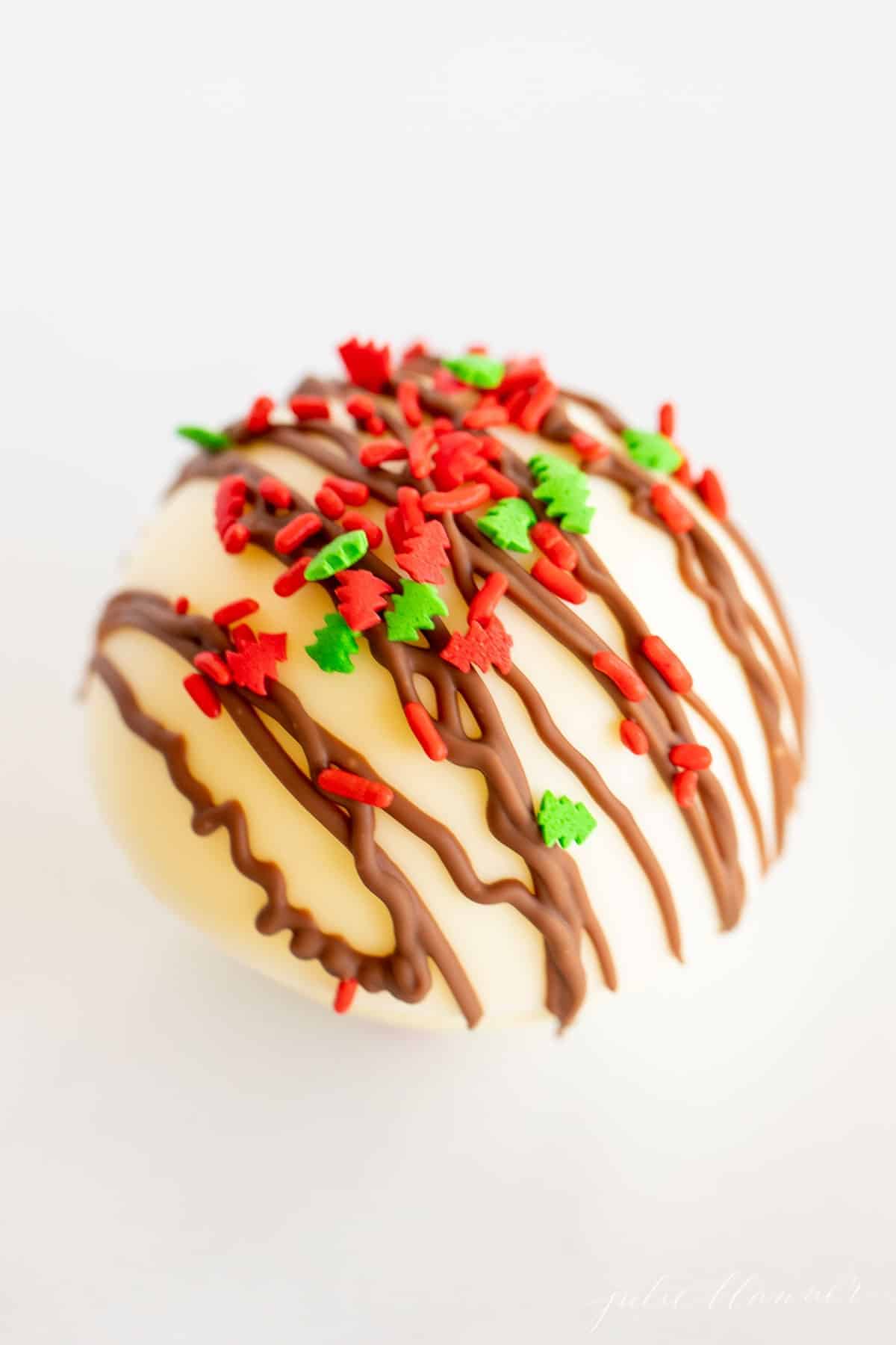 一个白色的盘子，上面有一颗白巧克力热巧克力炸弹，上面有圣诞糖屑。gydF4y2Ba