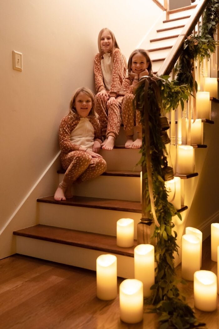 楼梯上的花环，周围都是蜡烛，三个小女孩穿着圣诞睡衣站在楼梯上