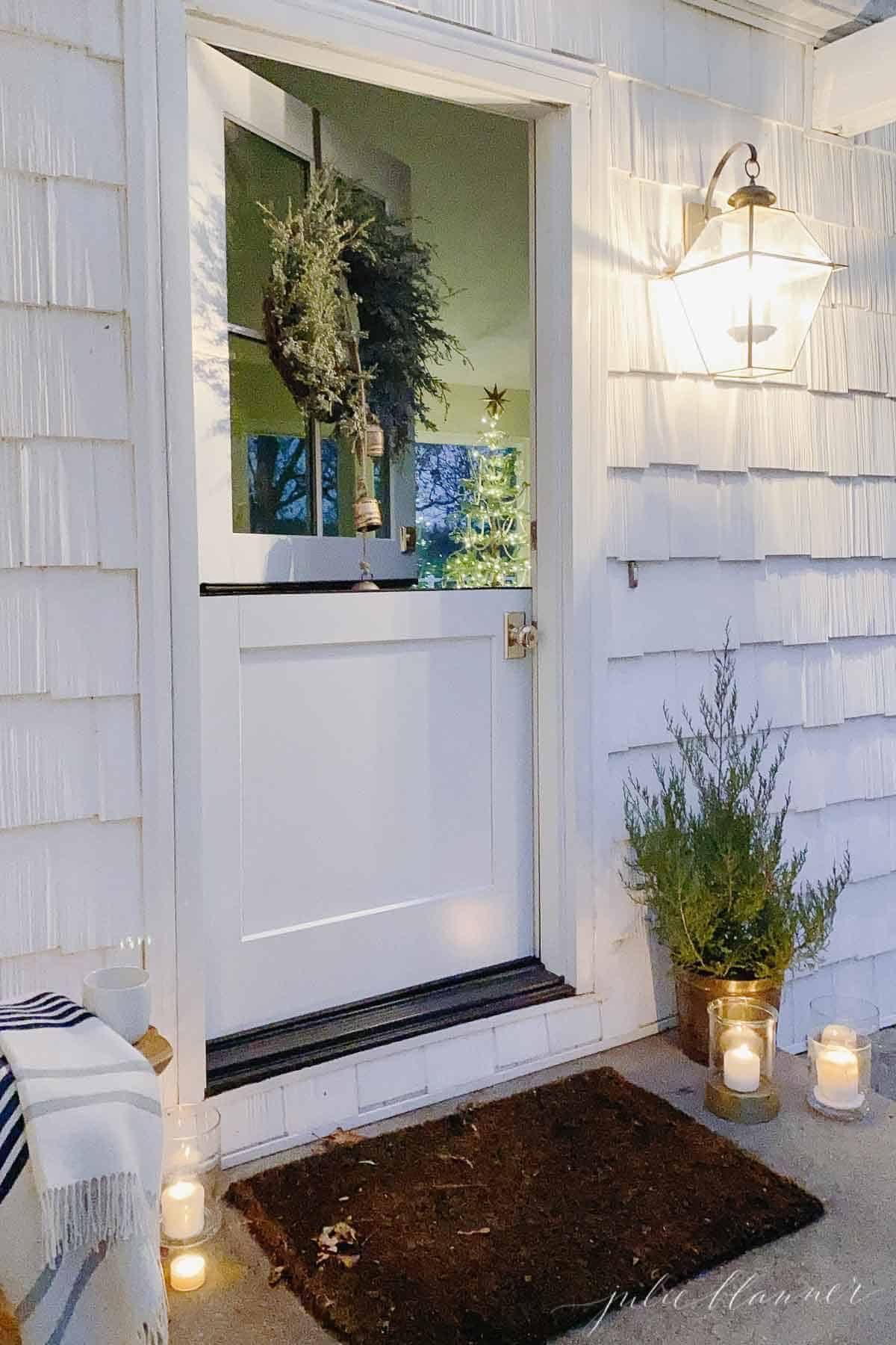 白色小屋上的一扇荷兰门，装饰着蜡烛和一棵迷你雪松树作为圣诞礼物。