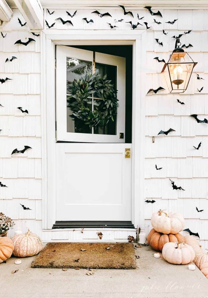 白色的荷兰门上的白色小屋房屋，南瓜和纸蝙蝠，周围是万圣节装饰。