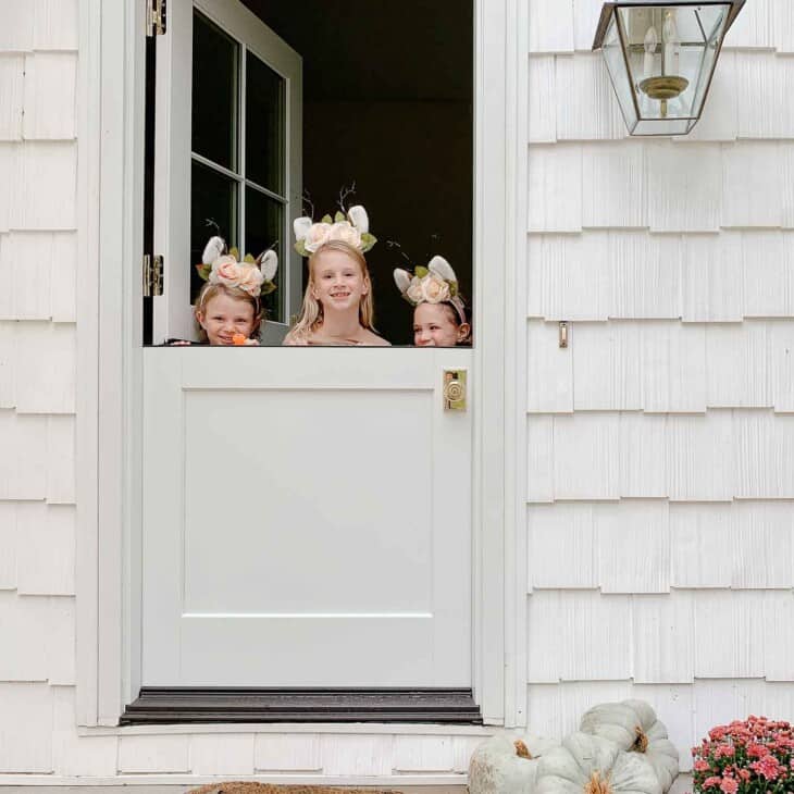一个白色的小屋，有一个白色的荷兰门，三个小女孩在顶部偷看。