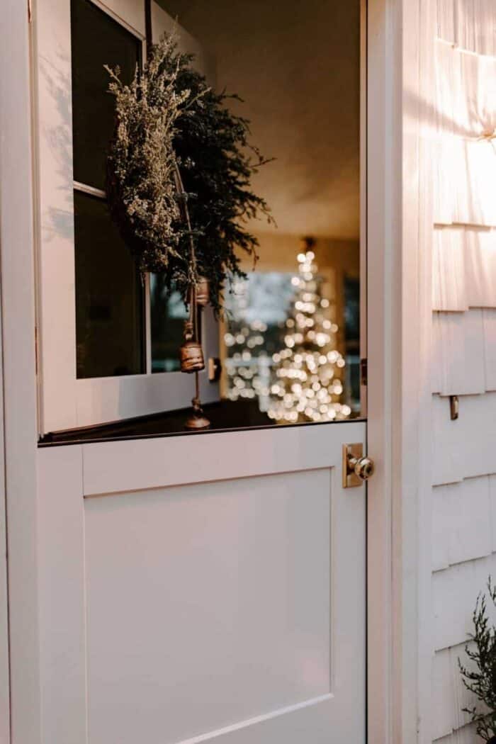 一扇白色的外部荷兰门，晚上打开，看着带有圣诞树的客厅。