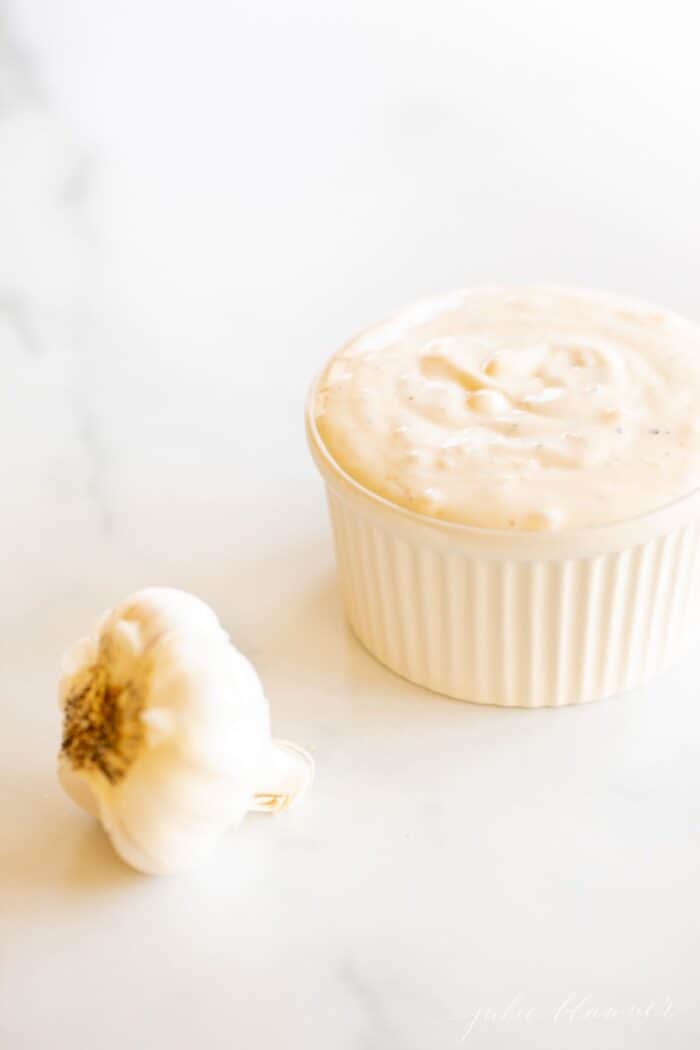 大理石台面上放着一个盛满新鲜蒜泥蛋黄酱的白色小模子盘，旁边放着一颗蒜头。