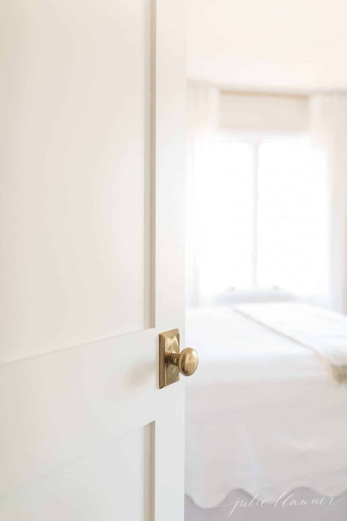 一个白色的振动筛样式门与黄铜门把手，开放到浴室里。