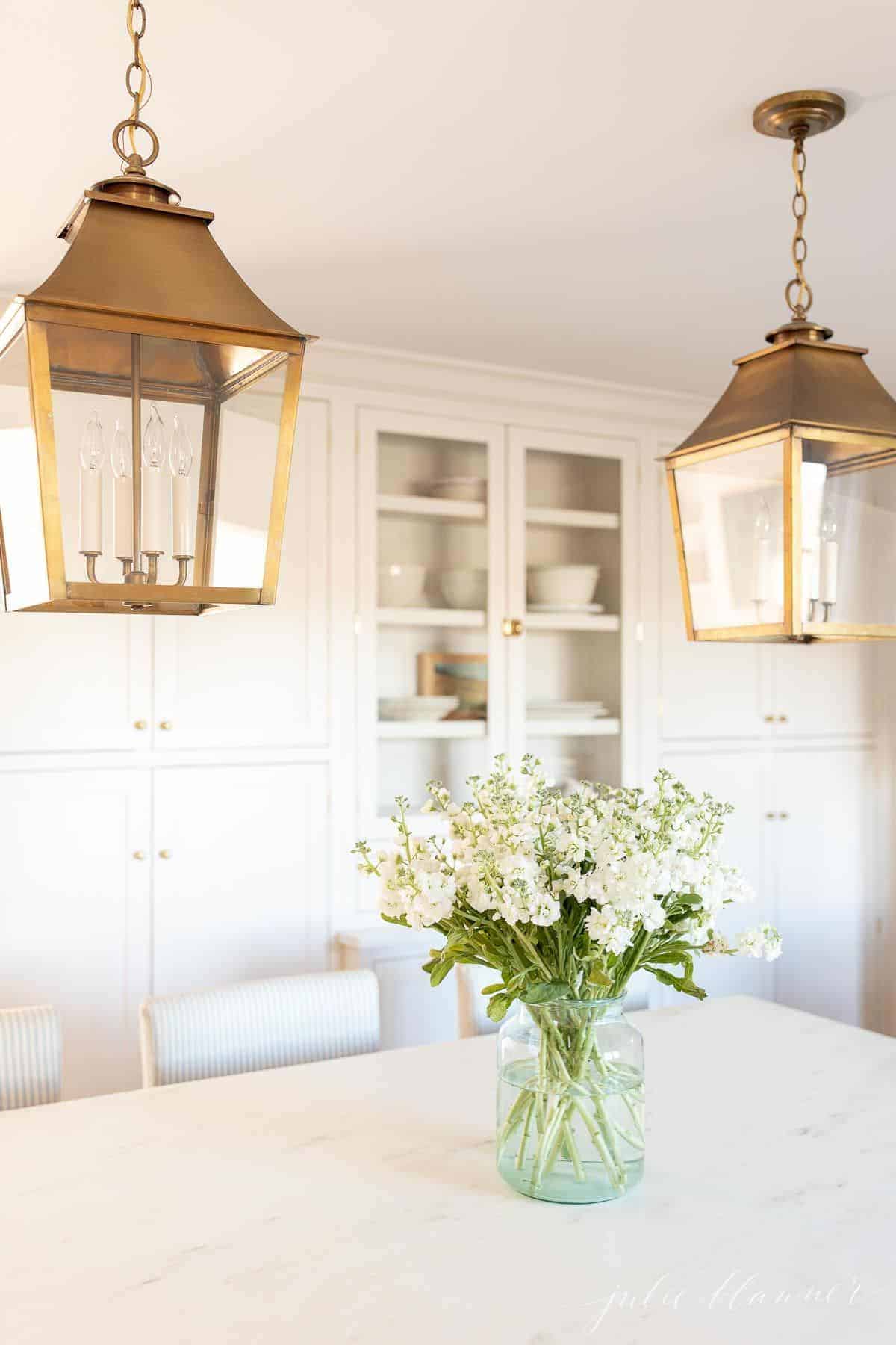 白色的厨房里有黄铜灯笼和大理石台面，岛上还摆放着原装鲜花。