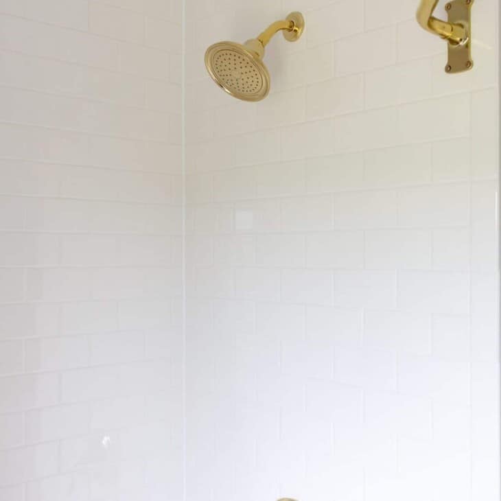 白色的地铁瓷砖淋浴，带有黄铜硬件。