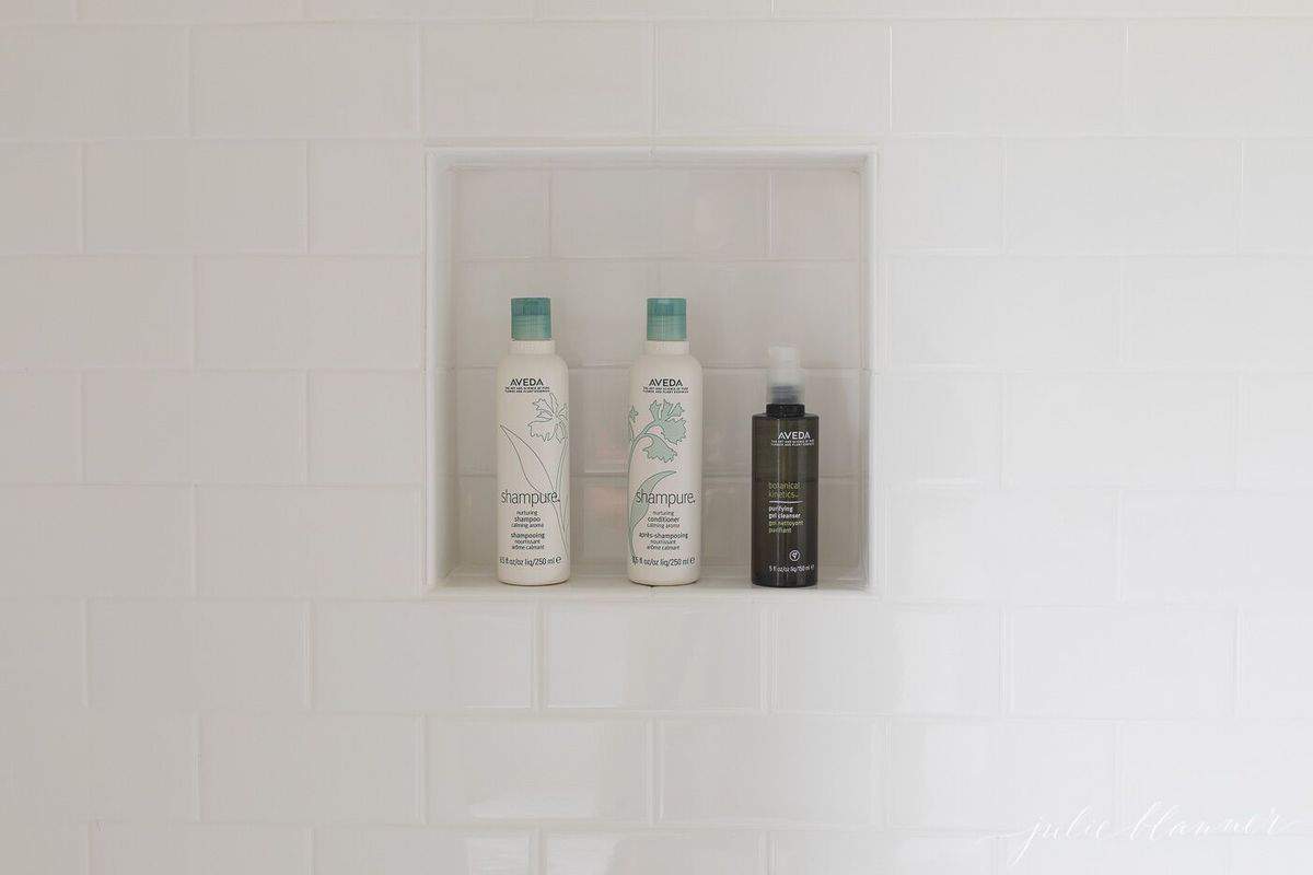 在铺着白色地铁地砖的浴室里，有一个放着洗发水瓶子的淋浴壁龛。