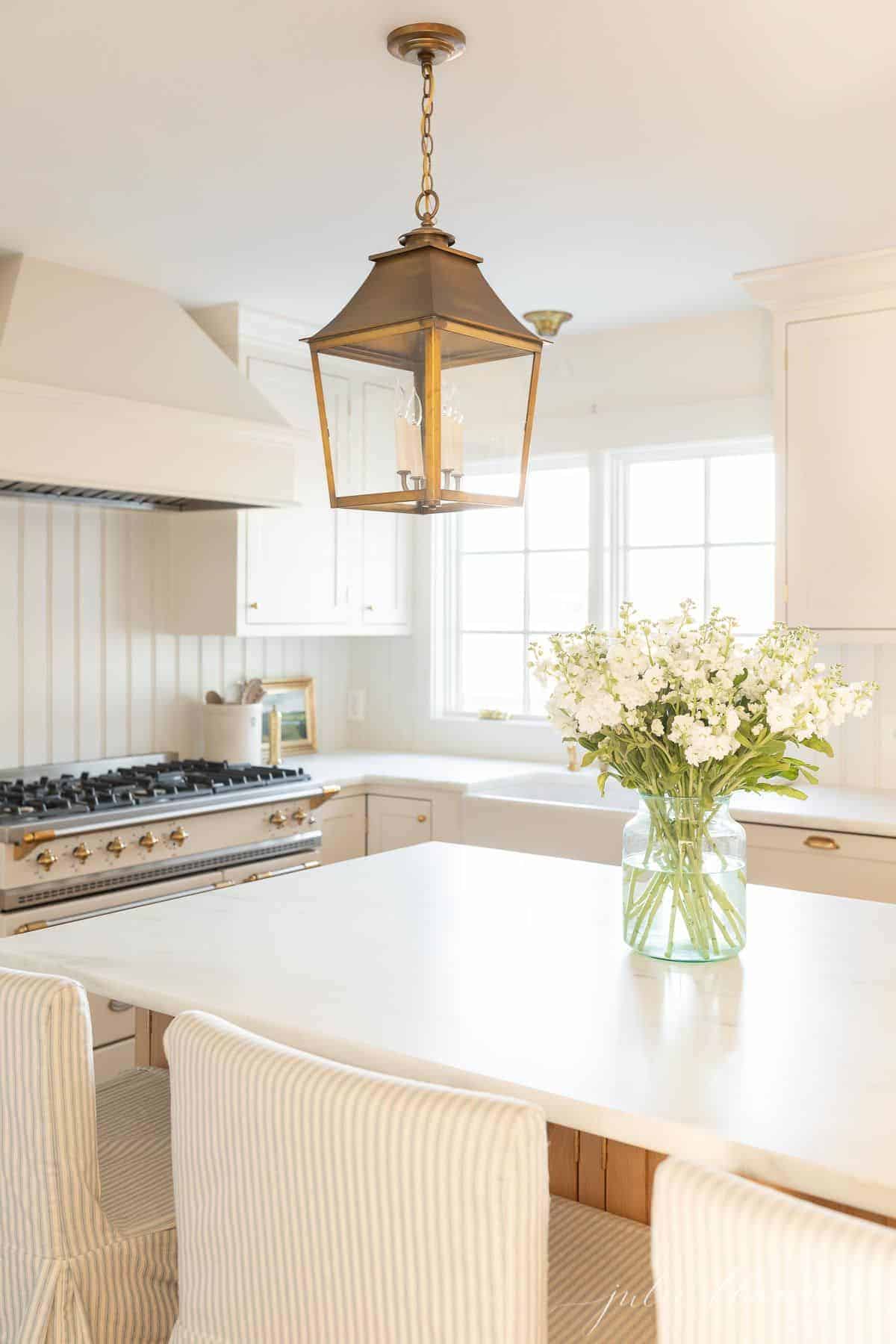 白色的厨房里有黄铜灯笼和大理石台面，岛上还摆放着原装鲜花。