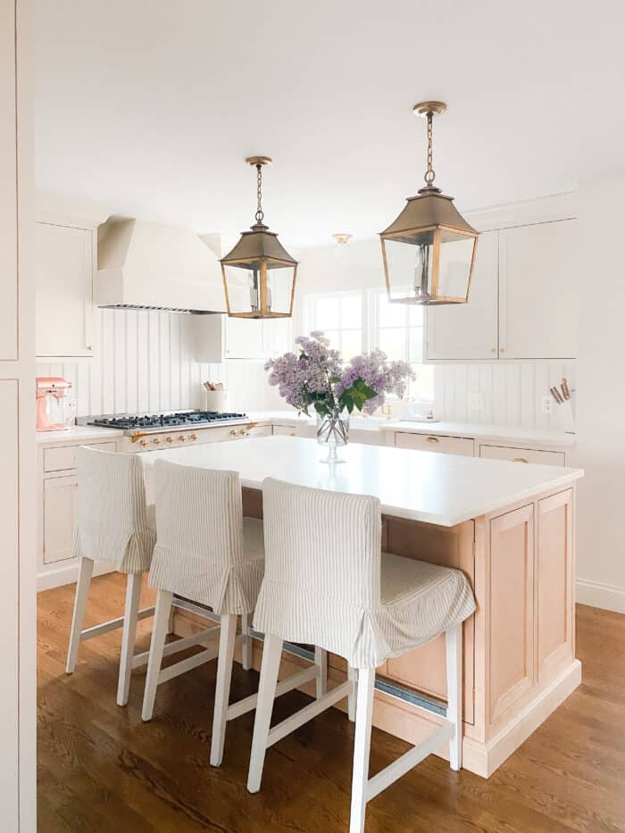 在一间带丹比(Danby)大理石台面的奶油色厨房里，黄铜灯笼挂在浅色的木质厨房岛上。