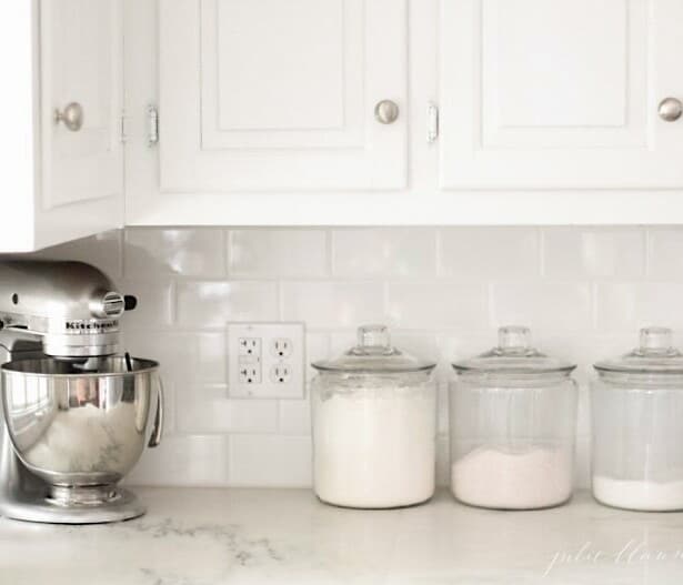 有大理石台面的白色厨房，烘烤用品的立场搅拌机和玻璃罐。