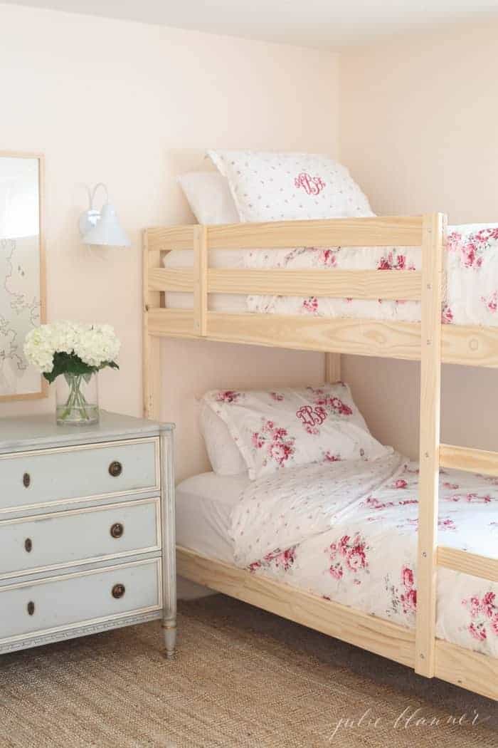 一个小女孩的卧室，有木制双层床，花床和淡粉色蛋壳漆的墙壁。
