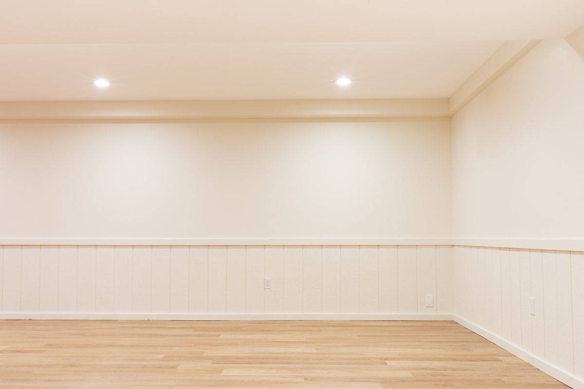 一个空的地下室，白色的墙壁和中色调的乙烯基木板地板。