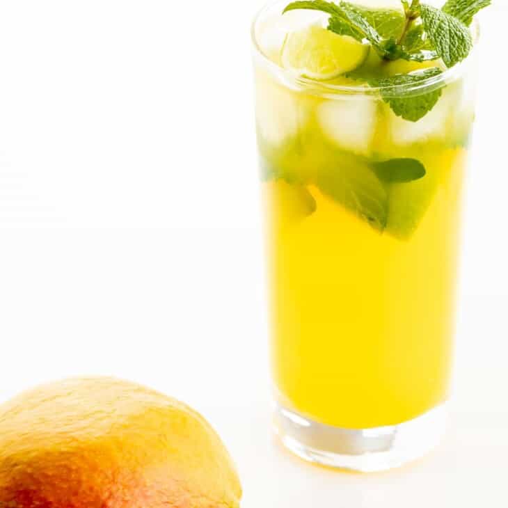 芒果莫吉托（Mango Mojito）的食谱在透明的玻璃杯中，上面饰有薄荷的小树枝，芒果在前景中。GydF4y2Ba