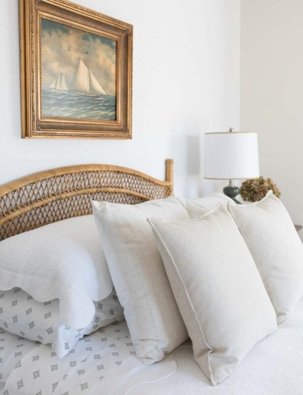 一间带中立床上用品的卧室，藤床和床头板上的帆船艺术品。