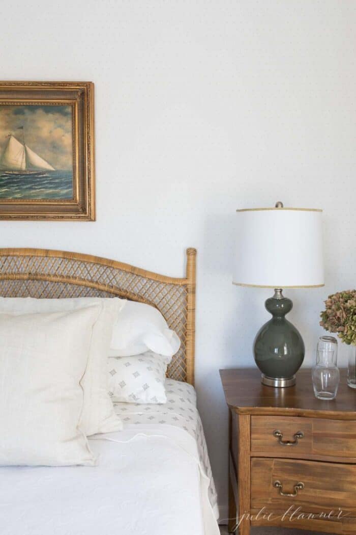 卧室里有中性的床上用品，一张藤条床，床头板上方有帆船艺术。
