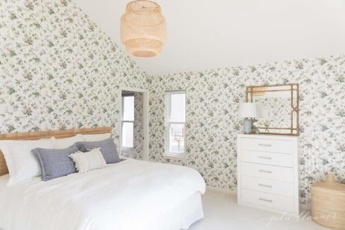 一间贴着碎花壁纸的卧室，里面有一张藤条床和白色的被褥。
