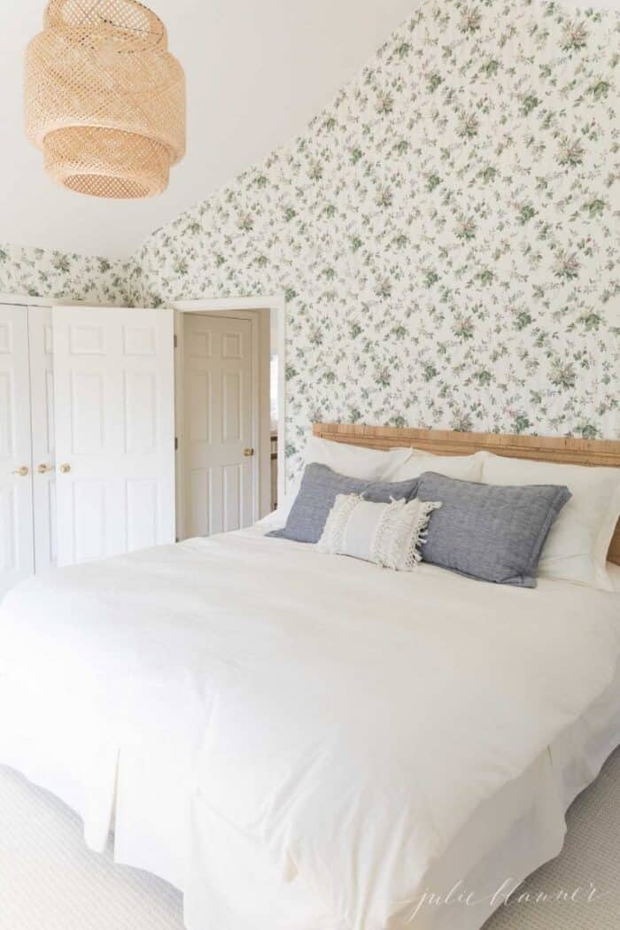 一间贴着碎花壁纸的卧室，里面有一张藤条床和白色的被褥。