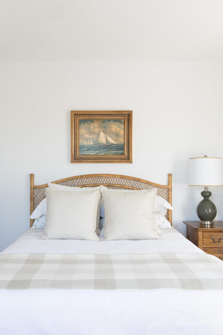 卧室里有中性的床上用品，一张藤条床，床头板上方有帆船艺术。