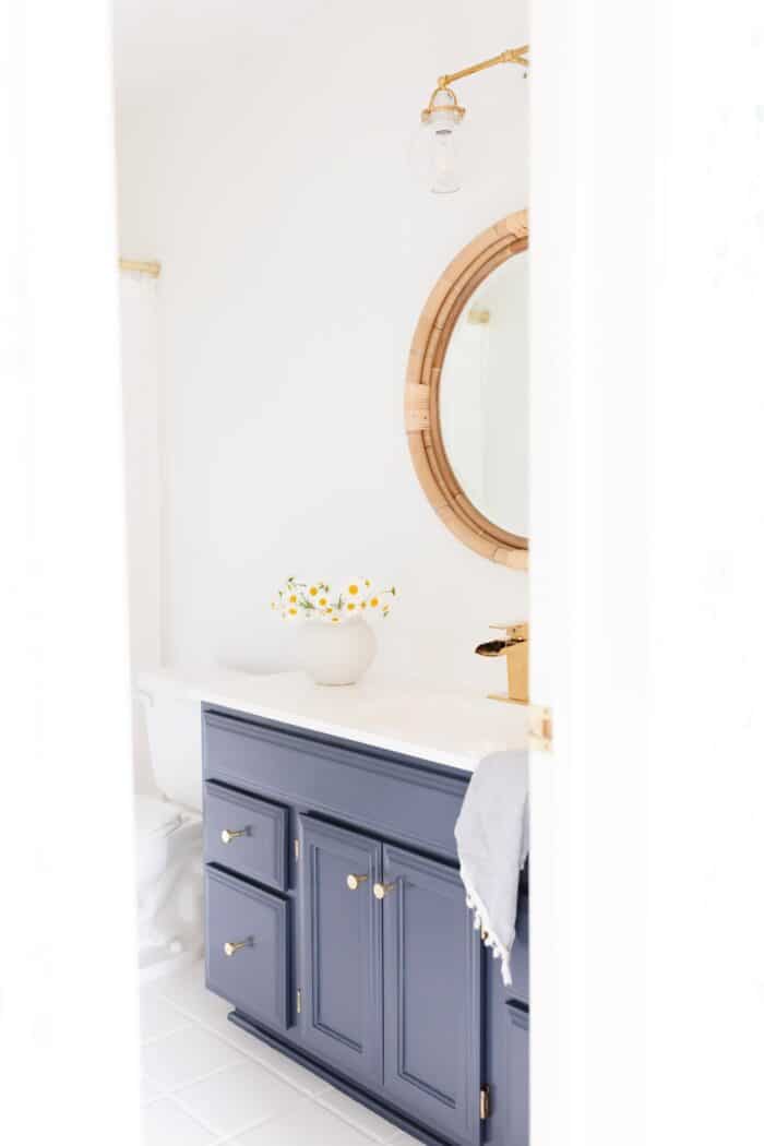 一个航海风格的浴室，白色的墙壁和一个用本杰明摩尔黑尔海军油漆颜色粉刷的木质梳妆台。