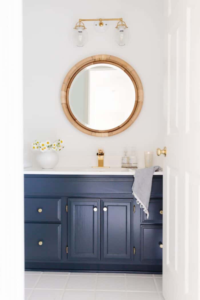 一间白色的浴室，有一面圆形的藤镜和一个深蓝色的梳妆台，用HC-154漆的。