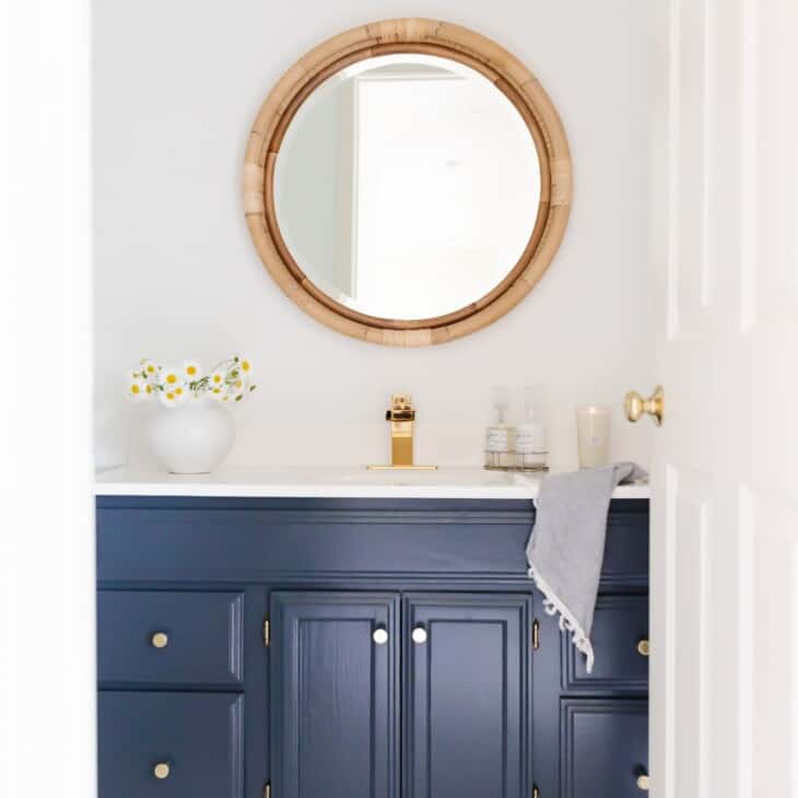 一间带有圆形藤制镜的白色浴室和深蓝色的洗手盆。