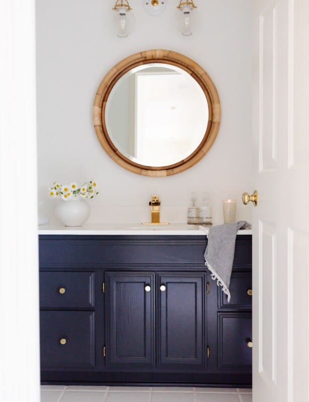 一间白色的浴室，有一面圆形的藤镜和一个深蓝色的梳妆台。