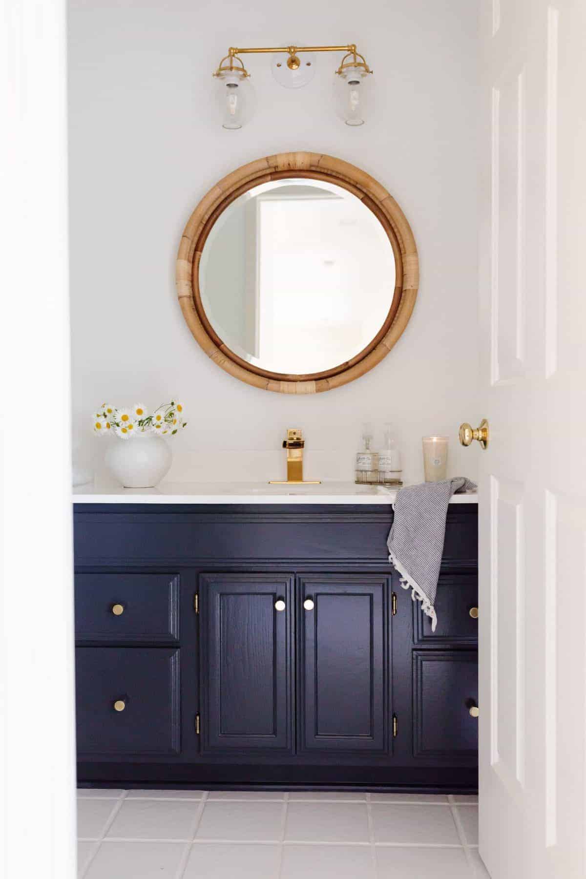 一间白色的浴室，有一面圆形的藤镜和一个深蓝色的梳妆台。