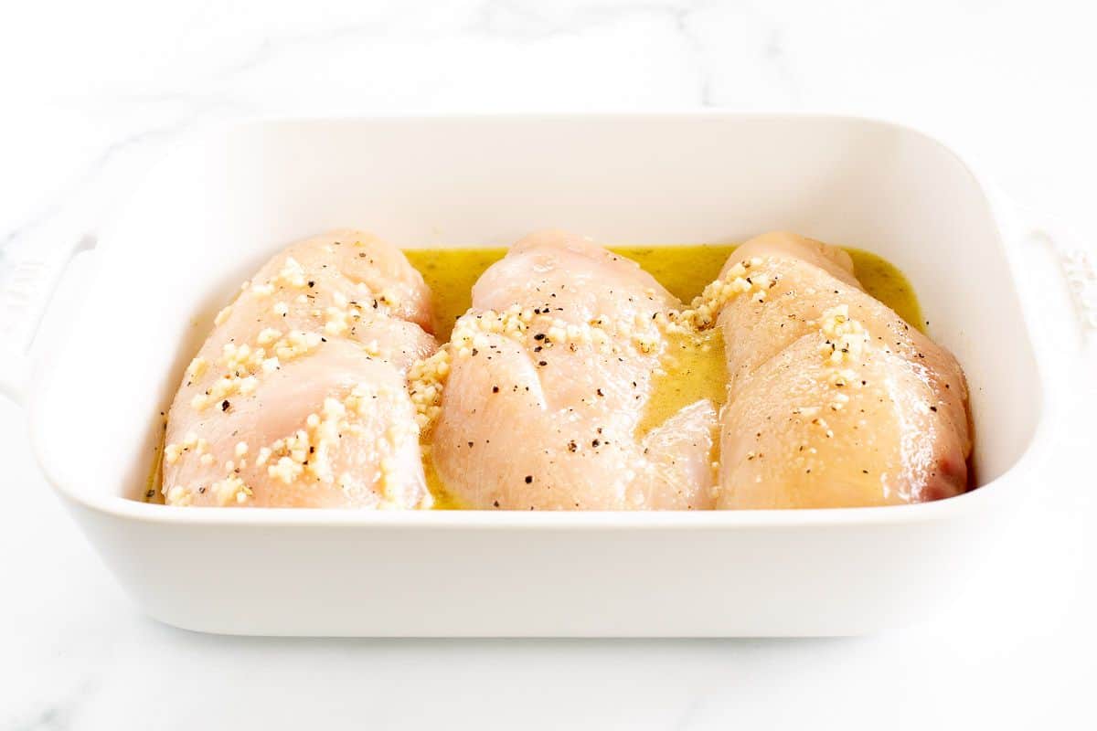 生鸡胸肉在白色平底锅中淋上橄榄油和调味料。gydF4y2Ba