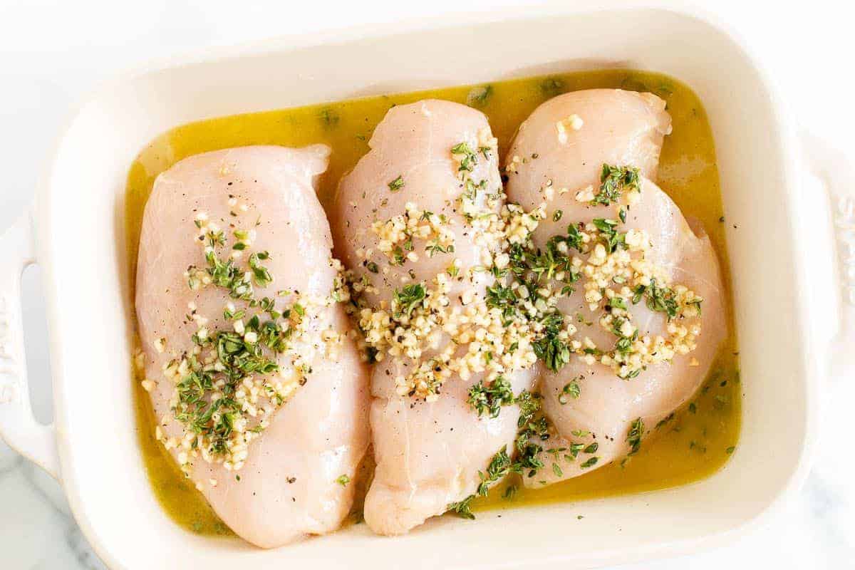 希腊腌鸡胸肉放在白色烤盘里，涂上希腊腌鸡肉汁。gydF4y2Ba