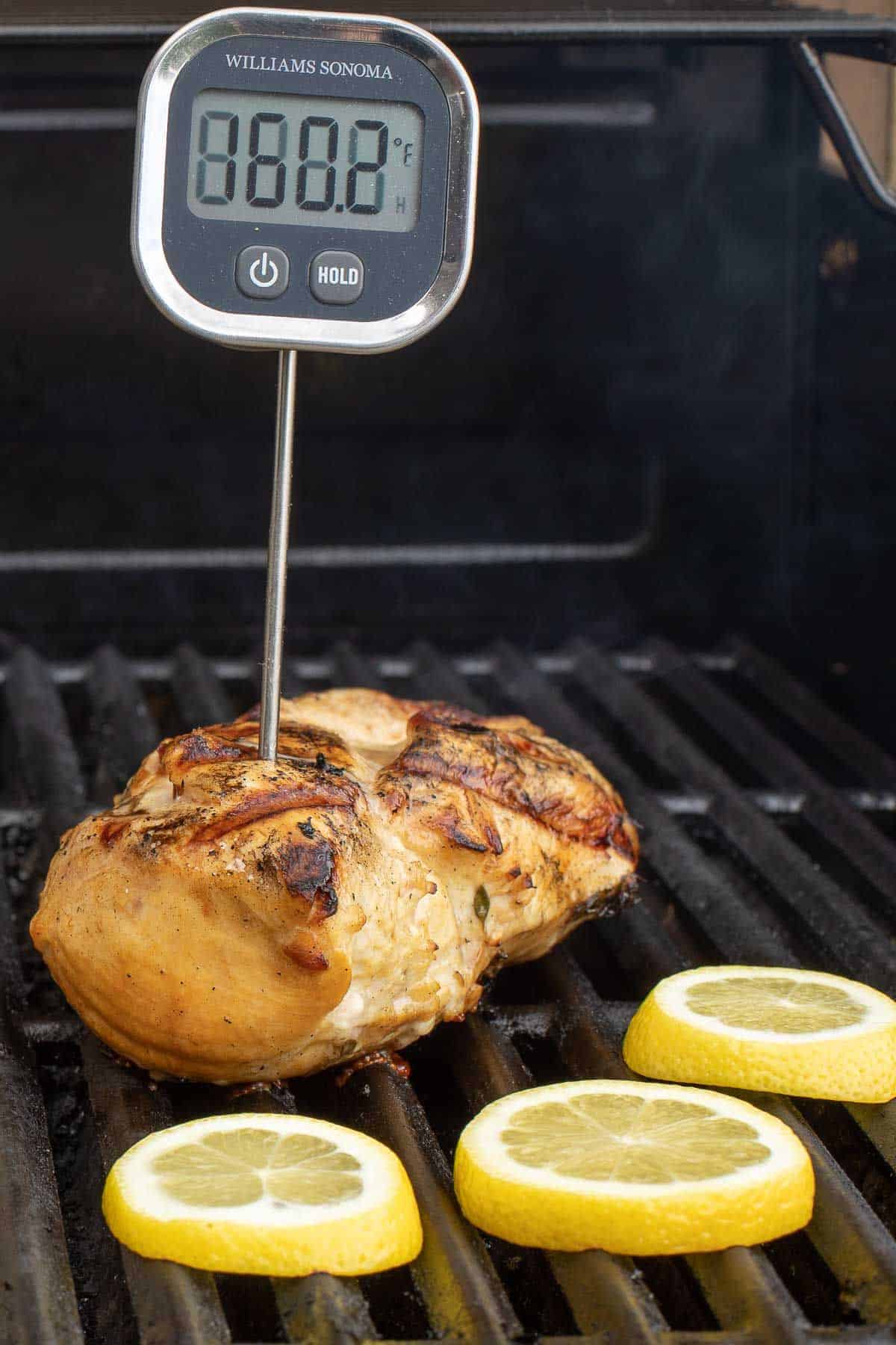 希腊鸡胸肉放在烤架上，肉温度计伸出来，柠檬片也烤着。